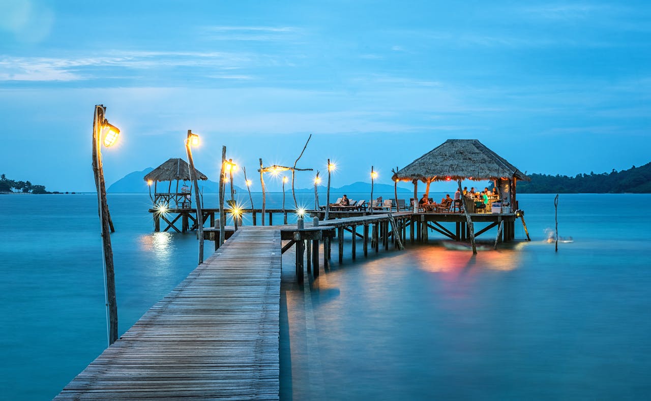 our-services-03 Illuminated pier and bungalow on a tranquil tropical sea at twilight.