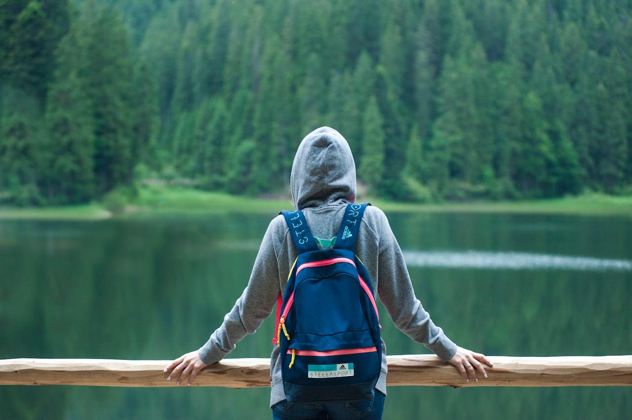 cta-image A person in a hoodie stands by a serene lake surrounded by lush greenery, enjoying the peaceful outdoors.