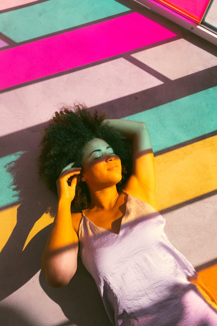about-us-img Woman relaxing on a colorful sunlit floor with shadows creating vibrant patterns.